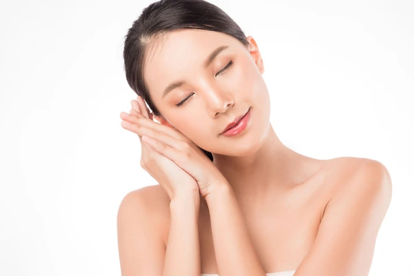 Młoda, uśmiechnięta kobieta z zamkniętymi oczami, z dłońmi ułożonymi w geście snu